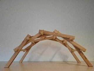 Das Bild zeigt eine kreative Holzstruktur in Form einer Bogenbrücke. Sie besteht aus mehreren miteinander verbundenen Holzleisten.
