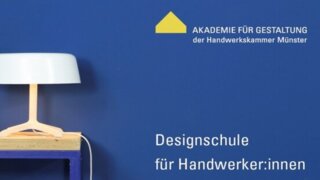 Das Bild zeigt eine moderne Tischlampe auf einem Holztisch vor einer blauen Wand. Daneben stehen Werkzeuge und Materialien für Handwerker:innen.