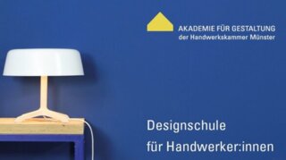 Das Bild zeigt eine moderne Tischlampe auf einem Holztisch vor einer blauen Wand. Daneben stehen Werkzeuge und Materialien für Handwerker:innen.